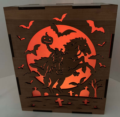 Halloween-themed decorative box with a headless horseman in a graveyard with a pumpkin for a head, and bats against an orange moonlit sky.
